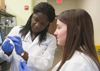 A professor and a student examine a vial in a pharmacy lab